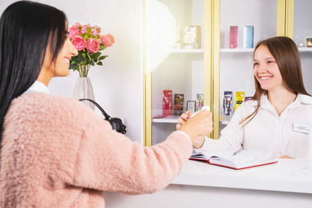 Business woman wearing pink sweater with black long hair smiling giving to her office manager young girl blond a gift certificate.の写真素材