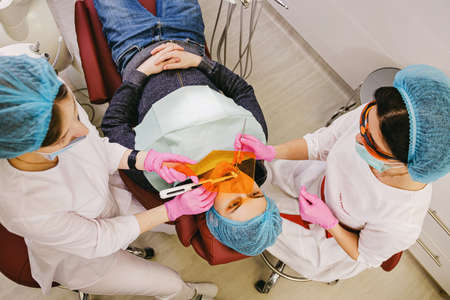 Photo from above of a patient receiving procedure of dental treatment by two doctors dentists in modern stomatology clinic.の写真素材