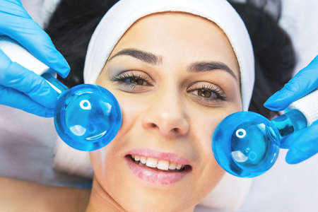 Close up photo of a woman undergoes the rejuvenation facial massage procedure in a beauty salon with ball roller tools.の写真素材