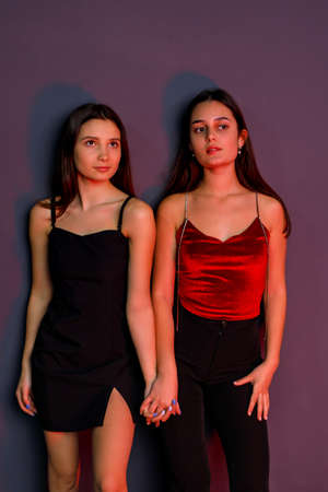 Full length photo of two elegant young women holding hands wearing black short dress and black trousers.の写真素材