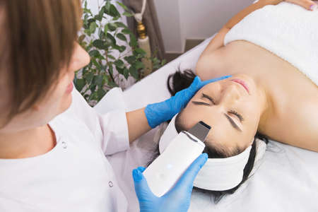 Specialist cosmetologist making facial procedure treatment to a patient woman using ultrasonic skin equipment.の写真素材