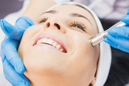 Closeup photo of smiling woman receiving face cleaning procedure in cosmetology clinic, vacuum cleaning.の写真素材