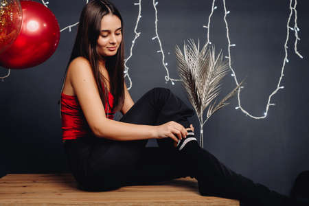 Close up of a beautiful girl in evening clothes sitting on the table straightens the black sock over grey background with red balloons and illumination.の写真素材