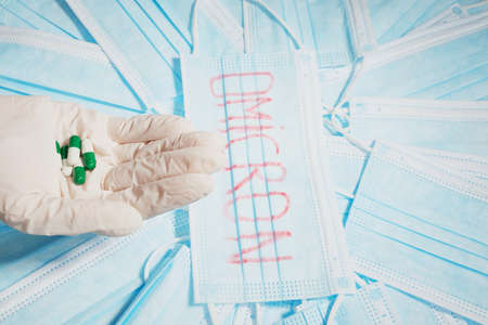 Photo of many medical masks with a word omicron virus written on one mask and a hand in glove holds tablets.の写真素材