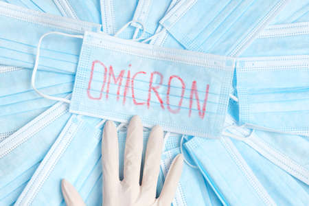 Variant of the covid 19 virus, omicron is written on a medical mask with part of a hand in glove surrounded by many masks.の写真素材
