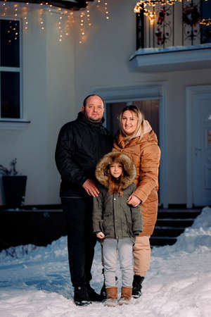 Full-length photo of a lovely family of three persons standing in front of their house, Merry Christmas and happy holiday.の写真素材