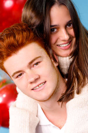 Close up photo of a beautiful young couple red hair boy and a brunette girl happy smiling on the camera over blue background with red balloons.の写真素材