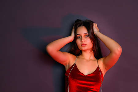 Fashion model young woman in colorful bright lights posing in sexual red clothes holding her hands on the head.の写真素材