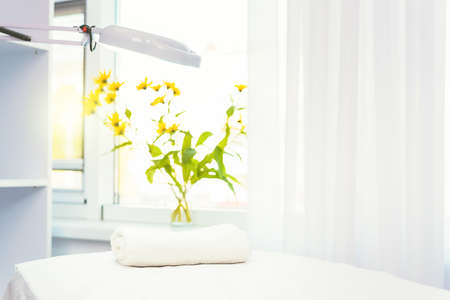 Close up photo of a cosmetologist empty office with care cosmetics and massage table with magnifying lamp and yellow natural flowers.の写真素材