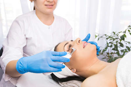 Beauty salon, doctor in blue gloves doing dermatologic procedures with ultra sonic scraber to a beautiful woman.の写真素材