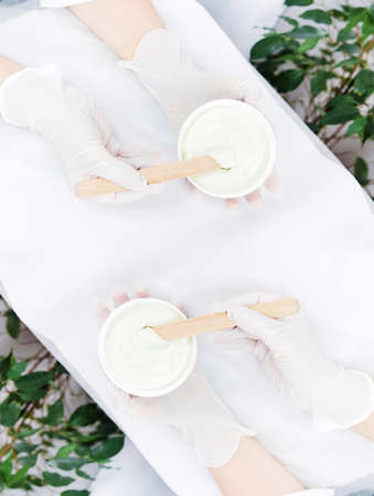 Photo from above of beauticians hands holding bowls and sticks preparing face rejuvenation cream mask, cosmetic product in a clinic beauty salon, mirror effectの写真素材