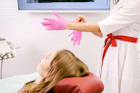 Young woman blond patient sitting on a dental chair in dentistry while woman dentist putting on gloves to start her work.の写真素材