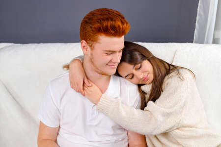 Beautiful wife putting her head on the shoulder of her red hair husband and relaxing together in the living room.の写真素材