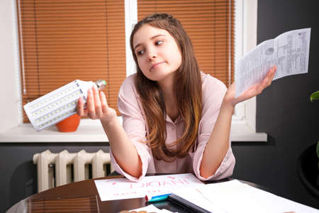 Young woman doing domestic accounting paperwork bills and invoices holding in her hand a payment for light and a bulb.の写真素材