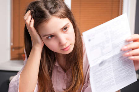 Close up photo of a young stressed woman looking at the invoices in her hand, domestic accounting paperwork bills and invoices.の写真素材