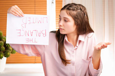 Young pretty woman showing with desperate her attitude to payments invoices and holding a paper with an inscription upside down.の写真素材