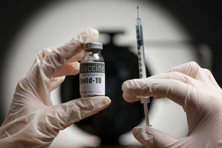 Doctor hands in gloves holding medical vial of vaccine and plastic syringe for injection on virus sign background.の写真素材