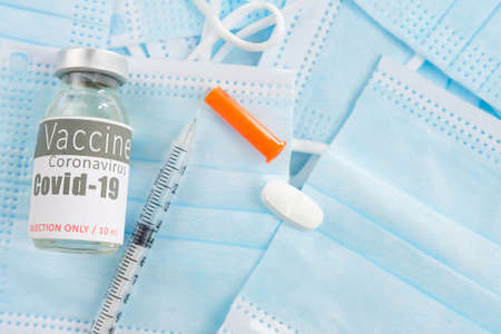 Photo of a vial of vaccine with a sterile syringe and remedy tablet against coronavirus and many medical masks.の写真素材