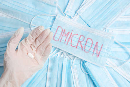 Photo of a hand in glove holds one tablet and many medical protective masks lying on the table with an inscription on one of omicron.の写真素材