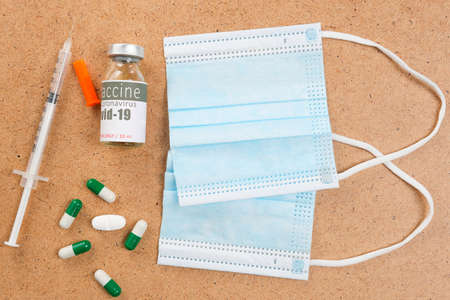 Close up photo of virus protective objects medical masks with a vial of vaccine and remedy tablets with syringe.の写真素材