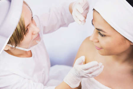 Top view photo of a woman client undergoes medical examination of the face by a cosmetician in gloves in beauty clinic.の写真素材