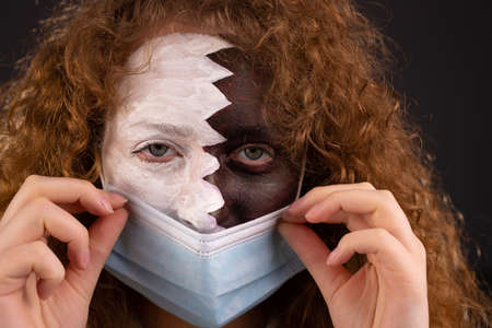 Portrait of a beautiful red-haired girl with blue eyes painted with the Qatar flag on her face has a medical mask on her face.の写真素材
