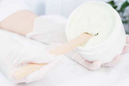 Close up photo of cosmetologist hands in medical gloves holding a jar of cream product scrab and tries to take it out of the jar in cosmetologist cabinet.の写真素材