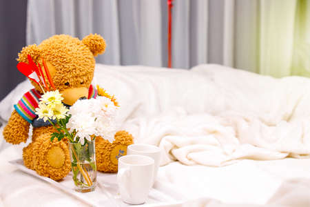 Amazing romantic breakfast in bed with two white cups, a vase of flowers and a bear toy for a couple, love concept.の写真素材