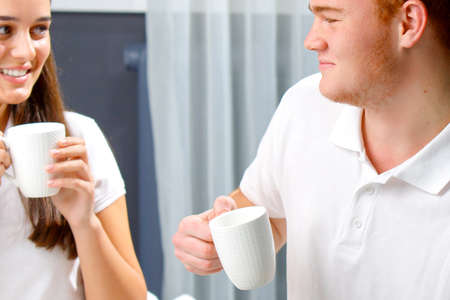 Young loving happy couple in white holding cups in their hands in the morning having breakfast, passing time together.の写真素材