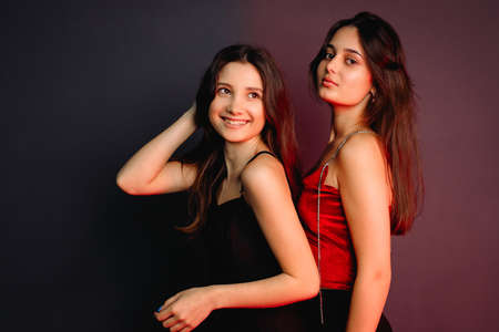 Side view photo of two beautiful self-confident young girls wearing elegant clothes, standing over the two colors background.の写真素材