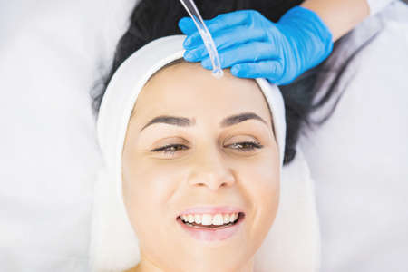 Beautiful woman receiving face cleaning procedure in salon skincare treatment by a professional cosmetologist.の写真素材