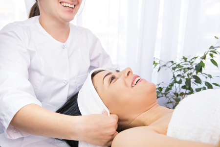 Cosmetologist laughing putting white headband towel on patient woman head for the face rejuvenation procedures in a beauty clinic.の写真素材