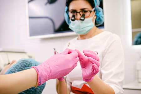 Blurred photo of a stomatology specialist woman doctor in dental loupe binoculars, medical gloves and mask taking some necessary tools from an assistant in dental clinic.の写真素材
