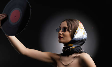 A photo of glamorous attractive young woman in sunglasses and beautiful shawl on a head holding vinyl LP in outstretched hand.の写真素材