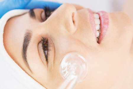 Horizontal close up photo of a beautiful woman smiling receiving rejuvenation facial procedure in a beauty clinic.の写真素材