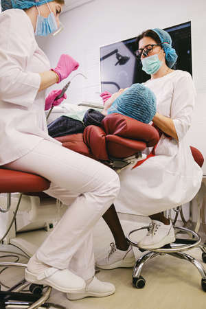 Dentists are working in modern stomatology clinic together with an assistant using stomatological instruments making teeth cure procedure to a patient man.の写真素材