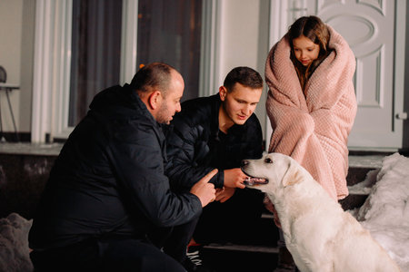 Happy family of two men and a little girl outside in winter clothes and blanket playing with their...