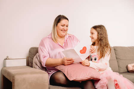 Little pretty girl prepared handmade post card with red painted heart symbol of unconditional love fo her mother.の写真素材