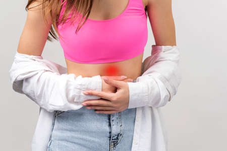 Cropped photo of a young girl in teenege clothes having stomach ache holding it with two hands, health care concept.の写真素材