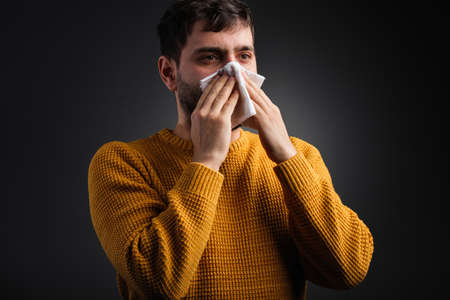 Close up photo of a man covering his nose with a handkerchief feeling bad and caught a cold, health care concept.の写真素材