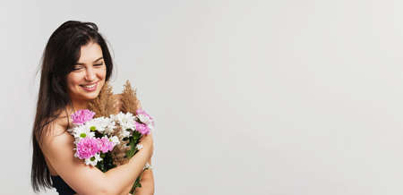 Smiling beautiful pretty lady brunette holds bunch of lovely flowers hiding her breasts on white background.の写真素材