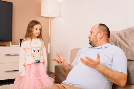 Close up photo of two persons man and little girl in the living room, girl standing and looking at her father while he explaining something to her.の写真素材