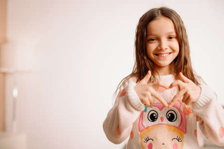 Smart lovely nice girl in a sweater with a drawing posing at the camera making heart sign using fingers.の写真素材