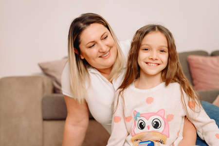 Daughter and mother sitting down on the carpet with smiling facial expression, mother looking at her daughter and girl looking at camera.の写真素材