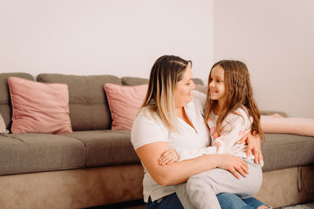 Mother sitting down on the floor and daughter sitting on mother knees looking at each other with love and tenderness.の写真素材