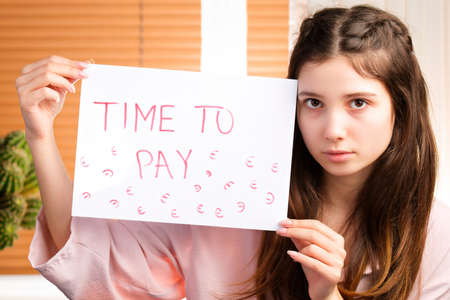 Young worried woman holding a paper in her hands with an inscription of time to pay, crisis in a bad financial situation.の写真素材