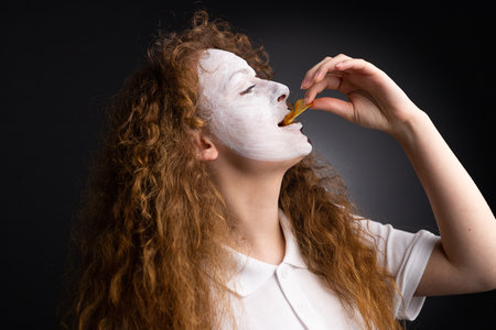Side view photo of a fan football woman in white t-shirt with painted face tasting chips on black background.の写真素材