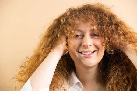 photo of cute beautiful funny young redhead woman playing with her hair looking at the camera and posing over golden background.の写真素材