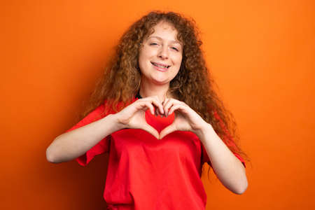 Picture of a smiling woman in soccer football uniform red color showing heart sign using two hands, football support concept.の写真素材