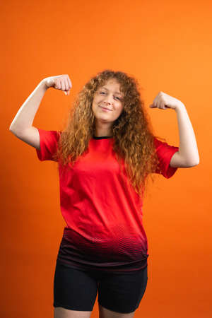 Strong redhead young woman fan of football in team uniform red and black color posing for the camera with satisfied facial expression.の写真素材